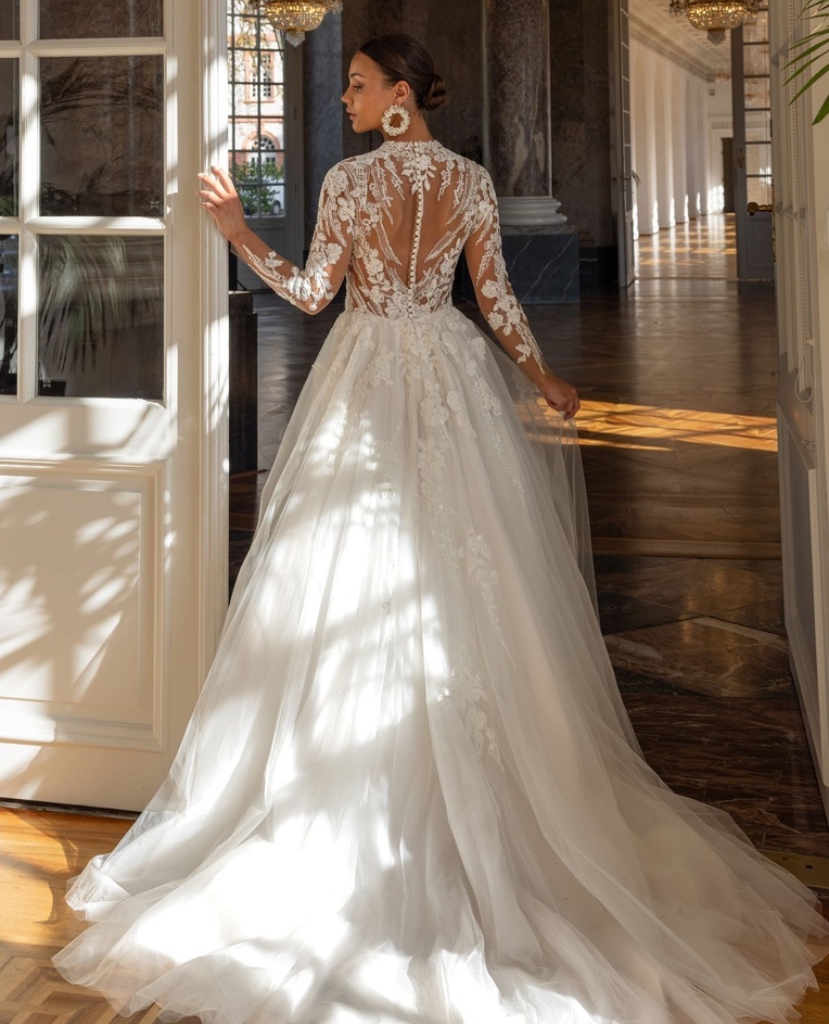Rückenansicht eines hochgeschlossenen A-Linien Brautkleides mit transparenter Spitze, Knopfleiste und fließender Schleppe, vom Brautladen Brittanja aus Moers.