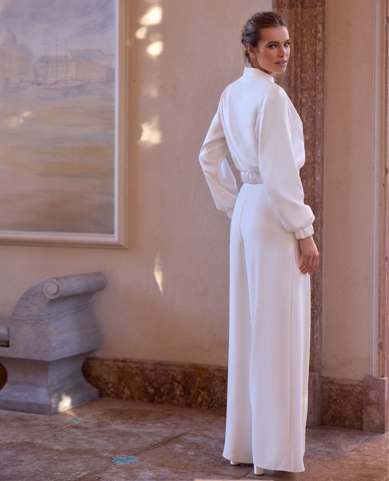 Minimalistischer Braut-Jumpsuit mit langen Ärmeln, hohem Kragen und betonter Taille für einen modernen Standesamt-Look, erhältlich bei Brittanja in Moers.