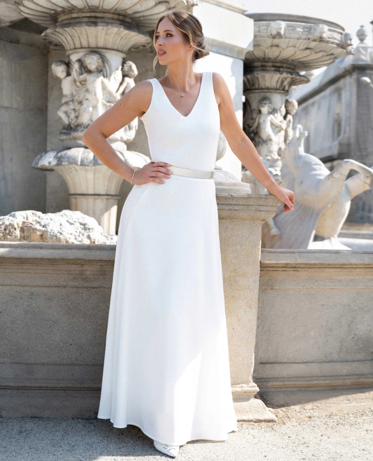 Puristisches, bodenlanges Standesamtkleid mit V-Ausschnitt und einem eleganten silbernen Taillengürtel, präsentiert vom Brautladen Brittanja in Moers.